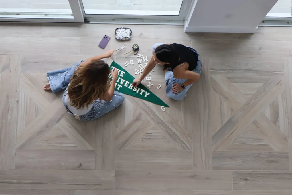 Alli and Amy laying out letter patches on a green University Edit pennant, seen from above