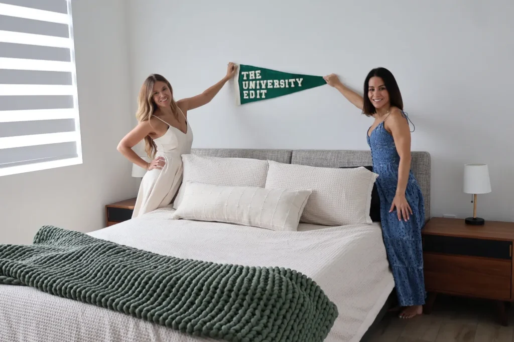 Alli (left) and Amy (right) of The University Edit hanging a green University Edit pennant above a styled bed